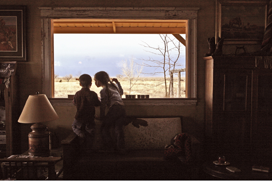Two children peering out of a western house window to the plains outside